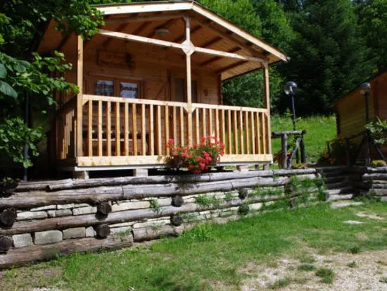 Bungalow in legno con veranda e gerani, su un muretto di tronchi