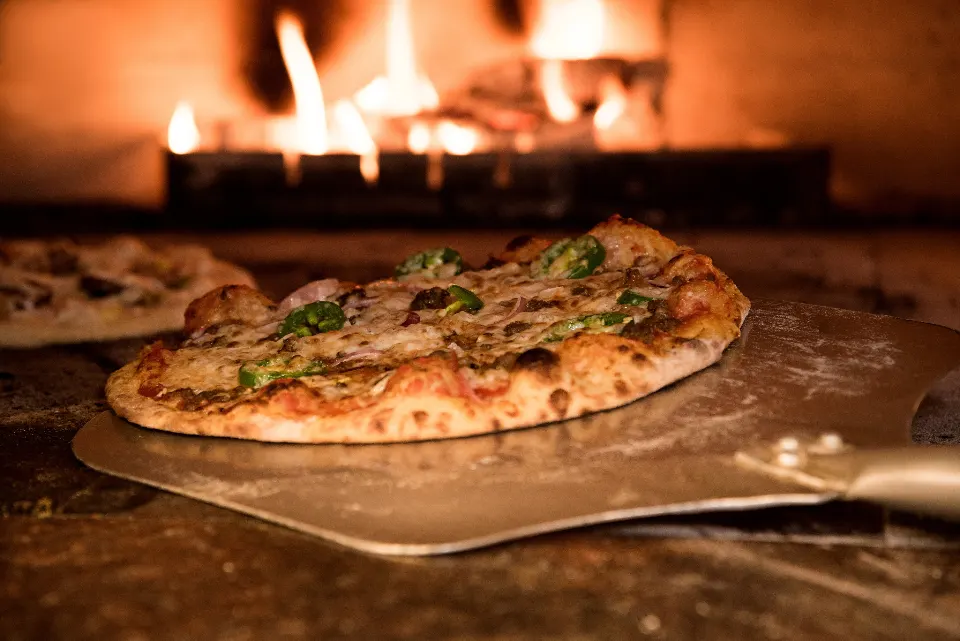Una pizza appena sfornata davanti al forno a legna